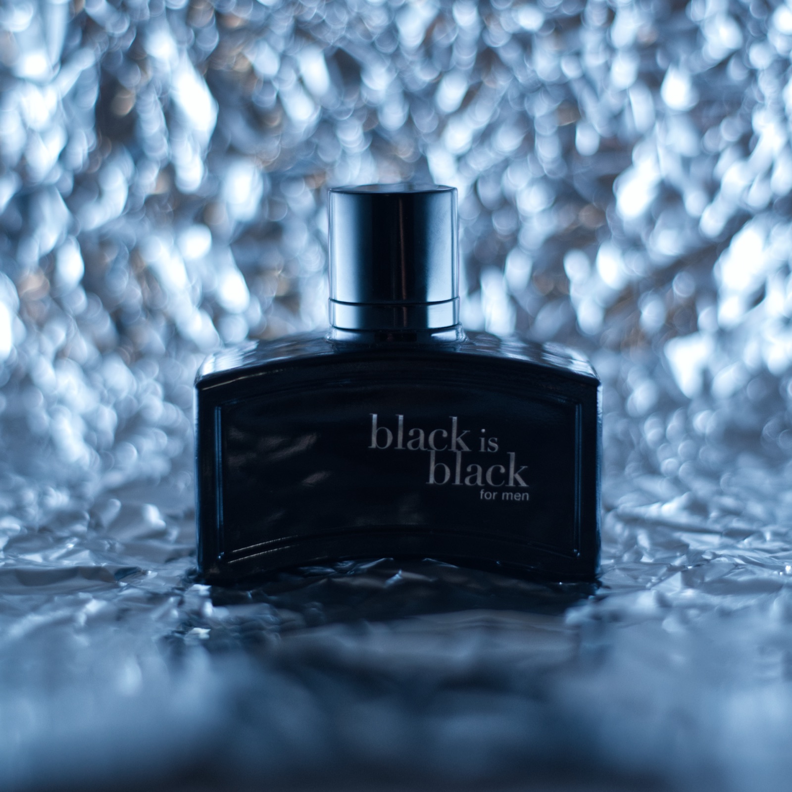 Frasco de perfume Black is Black sobre superficie texturizada plateada